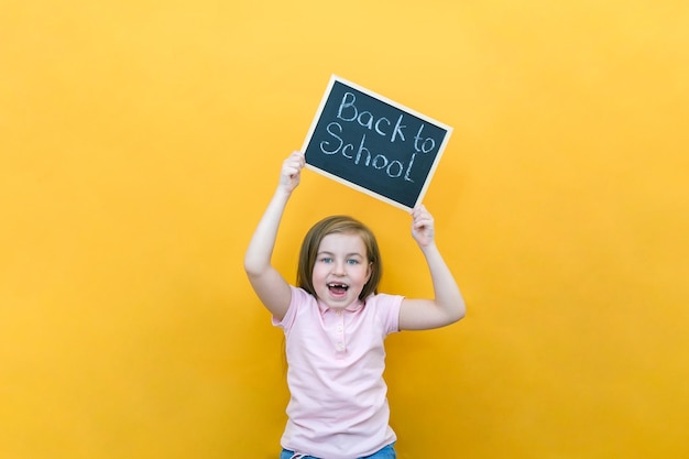 Schoolgirl holding a tablet in her hands with the inscription Back to school on a yellow background