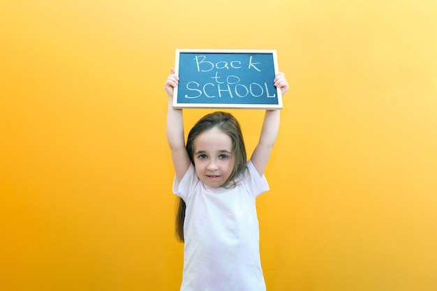 Schoolgirl holding a tablet in her hands with the inscription Back to school on a yellow background