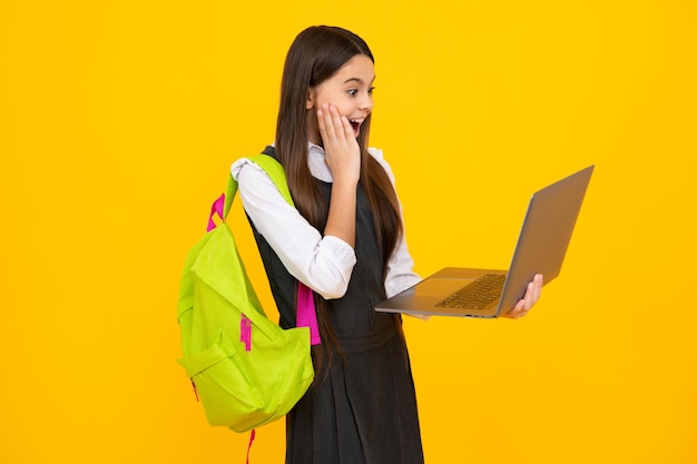 Schoolgirl in school uniform with laptop Schoolchild teen student on yellow isolated background