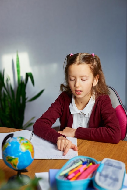 Schoolgirl sit at desk doing homework reading homeschooling Small junior girl engaged in distant learning get remote elementary education and preparing for exams