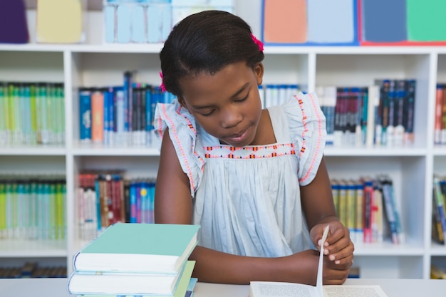 Schoolgirl sitting on table and reading book in library