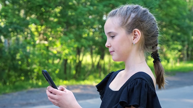 Schoolgirl types on phone standing on forest road closeup