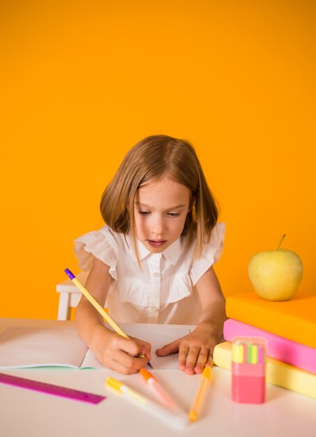 Schoolgirl in a uniform is sitting at a table and writing in a notebook on a yellow background with a place for the text