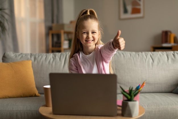 Schoolgirl Using Laptop Gesturing Thumbs Up Approving ELearning At Home