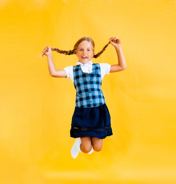 Schoolgirl with a backpack jumping on a yellow background