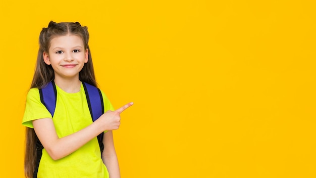 A schoolgirl with a backpack A little girl with a satchel on her back Supplementary education of the child Educational preparatory courses for school Yellow isolated background Copy space