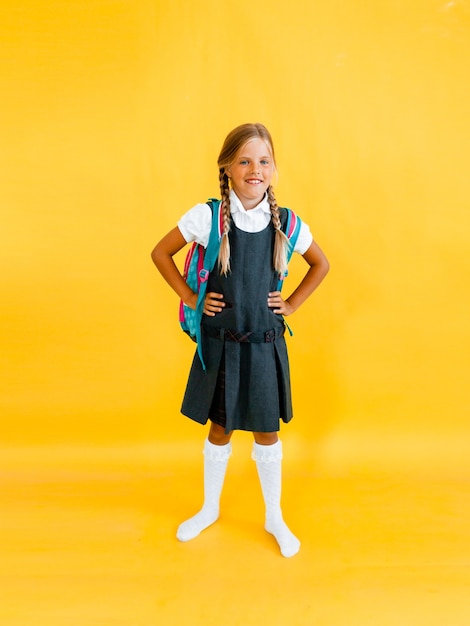 Schoolgirl with backpack stands and jumps on yellow studio background