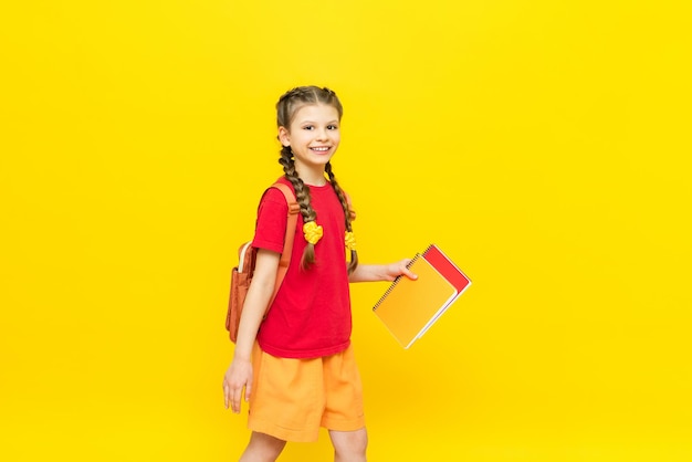 A schoolgirl with a backpack and textbooks Preparing a student for exams A little girl is going to school on a yellow isolated background Children's education