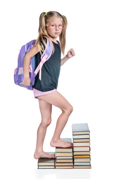 Schoolgirl with backpack walks up the stairs of books isolated on white background