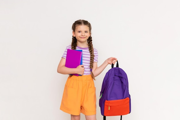 A schoolgirl with books holds a backpack in her hand on a white isolated background Preparation for the academic year