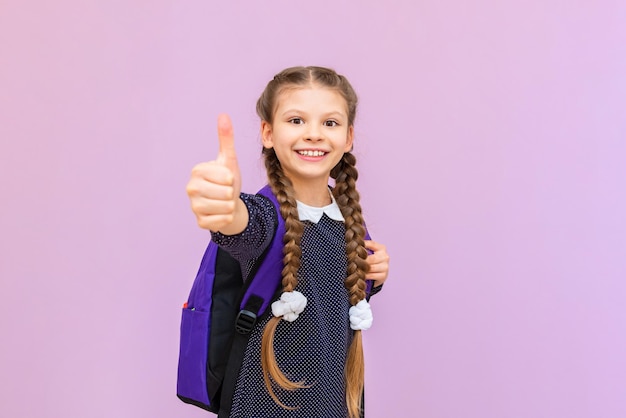 A schoolgirl with a briefcase gives a thumbs up and smiles a little girl with a briefcase on an isolated background