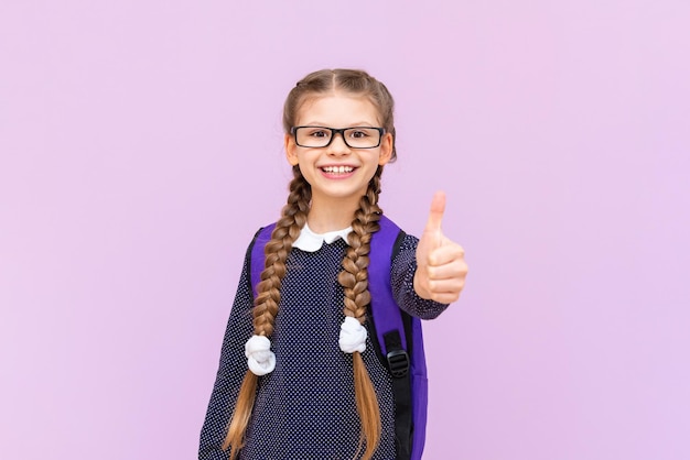 A schoolgirl with a briefcase and glasses on an isolated purple background primary school education at school courses for preparing children for school