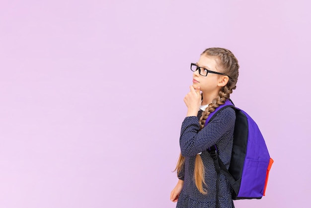 A schoolgirl with a briefcase and glasses on an isolated purple background primary school education at school courses for preparing children for school