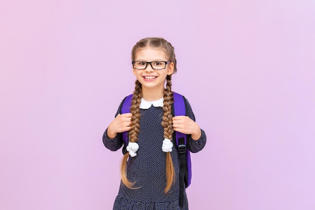 A schoolgirl with a briefcase and glasses on an isolated purple background primary school education at school courses for preparing children for school