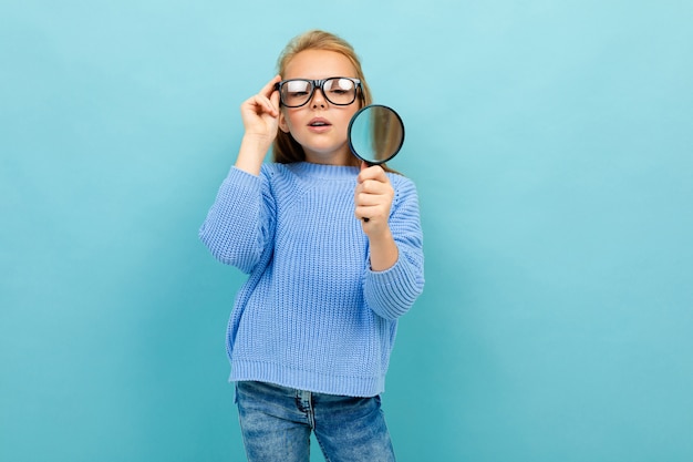 Schoolgirl with glasses and a magnifier on a blue background