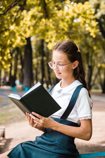 Schoolgirl with glasses reading a book on a warm day in the park Vertical view