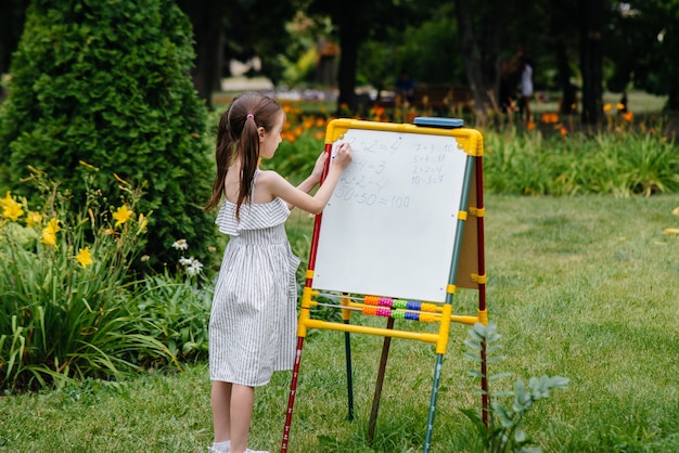 A schoolgirl writes lessons on a blackboard and is engaged in outdoor training. Back to school, learning during the pandemic.