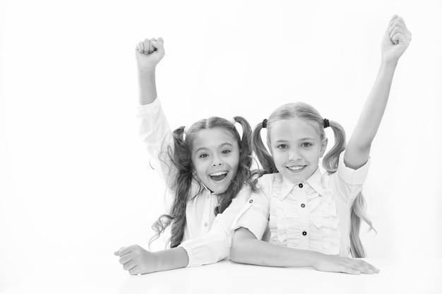 Schoolgirls happy keep hands up while sit at desk white background Win school quiz They know right answer Schoolgirls emotional cheerful celebrate victory Winners team Teamwork and leadership