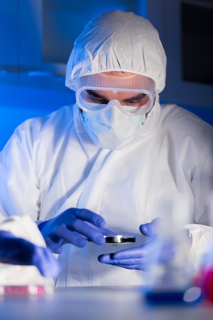 science, chemistry, biology, medicine and people concept - close up of male scientist in goggles and protective mask with test sample at chemical laboratory