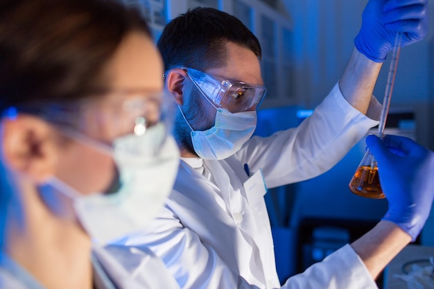 science, chemistry, biology, medicine and people concept - close up of young scientists with pipette and flasks making test or research in clinical laboratory