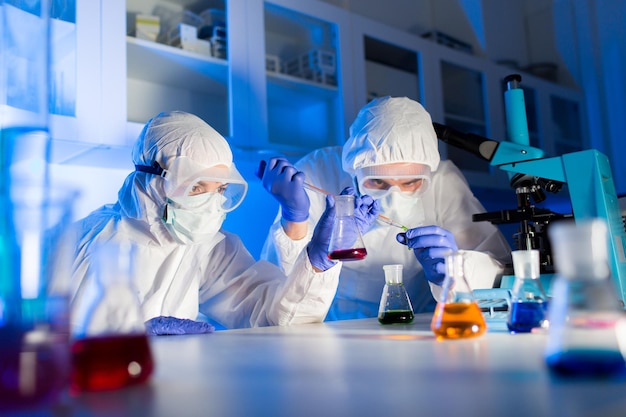 science, chemistry, biology, medicine and people concept - close up of young scientists with pipette and flasks making test or research in clinical laboratory