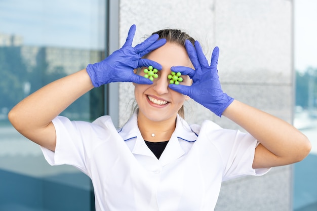 ScienÑe, chemistry, biology and medicine concept - Smiling European girl scientist in a white coat, goggles, and blue rubber gloves making eyes out of molecules on the street