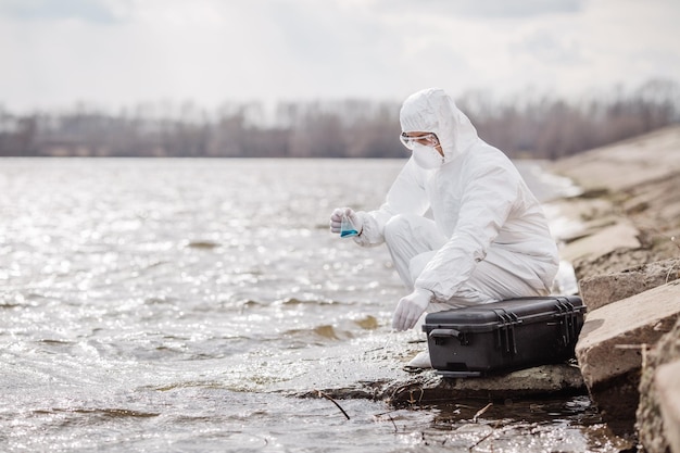 Scientist or biologist wearing protective uniforms examining the liquid contents of a test tube xA