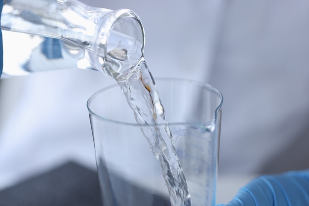 Scientist chemist pouring water from transparent bottle into flask in laboratory closeup