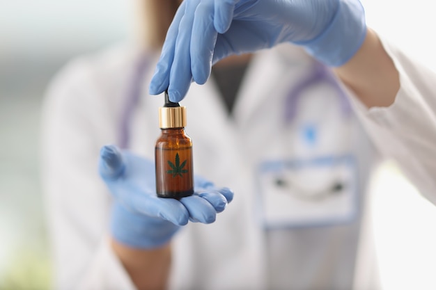 Scientist chemist in protective gloves holding hemp oil in jar closeup. Illegal production of narcotic drugs concept