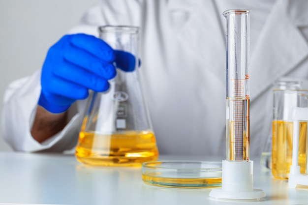 Scientist or doctor in blue gloves pouring some yellow liquid into a flask