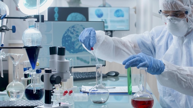 Scientist doctor wearing ppe equipment doing chemical experiment using medical transparent glasses mixing liquid solution during microbiology experiment in hospital laboratory. Medicine concept