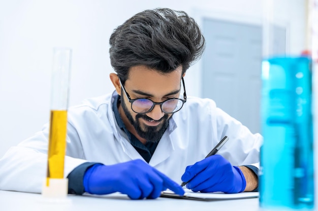 Scientist examining liquid in laboratory researchersitting at his workplace wearing lab coat