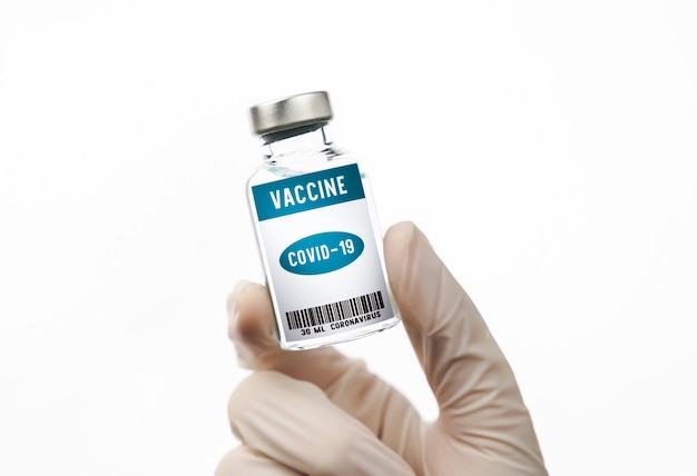 Scientist hand holding coronavirus vaccine in glass bottle on white wall.