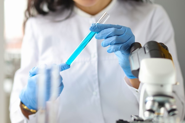 Scientist hands in gloves holds test tube with blue liquid in laboratory household chemicals