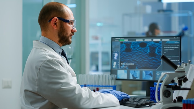 Scientist in lab coat analysing blood sample from test tube. Viorolog researcher in professional laboratory working to discover medical treatment, team of doctors analysing vaccine evolution