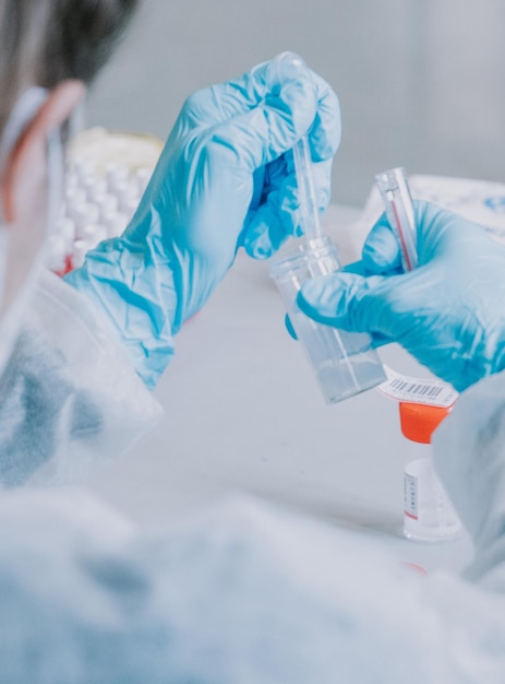 A scientist in a lab wearing a blue lab coat and gloves holds a test tube with a dropper