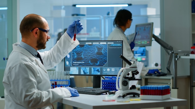 Scientist man examining blood samples and liquid working in modern equipped laboratory. Team of doctors analysing vaccine evolution using high tech researching diagnosis against covid19