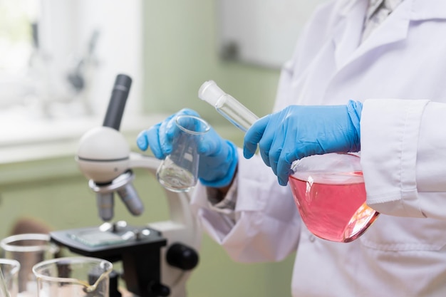 Scientist pouring pink substance from one flask to another in a laboratory during research work