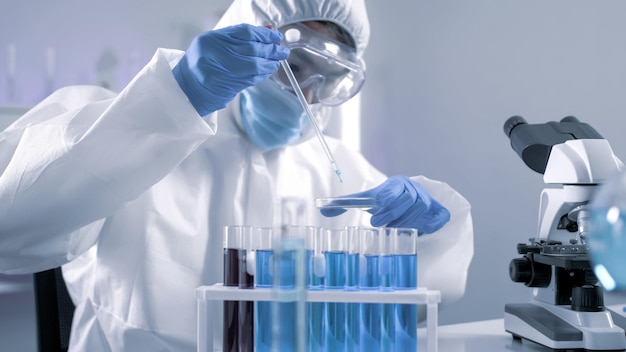 Scientist in PPE suite doing some research checking a liquid in a test tube at laboratory