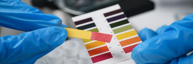 Photo scientist in rubber gloves compares indicator paper to color samples palette worker does