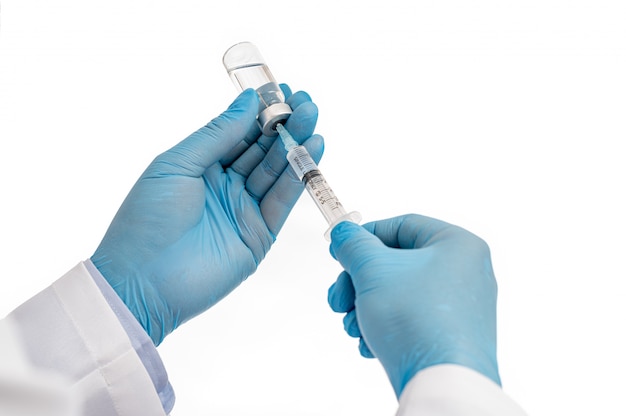 Scientist's hand wearing blue gloves against white background and holding Covid-19 vaccine.