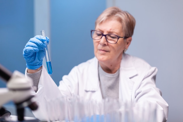 Scientist senior woman looking into test tube for biochemistry test