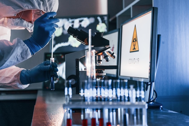 Scientist in white protective uniform works with coronavirus and blood tubes in laboratory