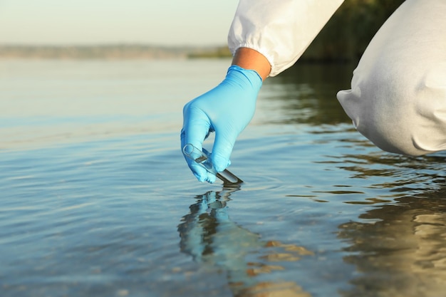 Scientist with test tube taking sample from river for analysis closeup