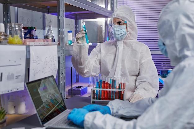 Scientists in protective suits examining liquid in test tubes in teamwork during their work in danger zone