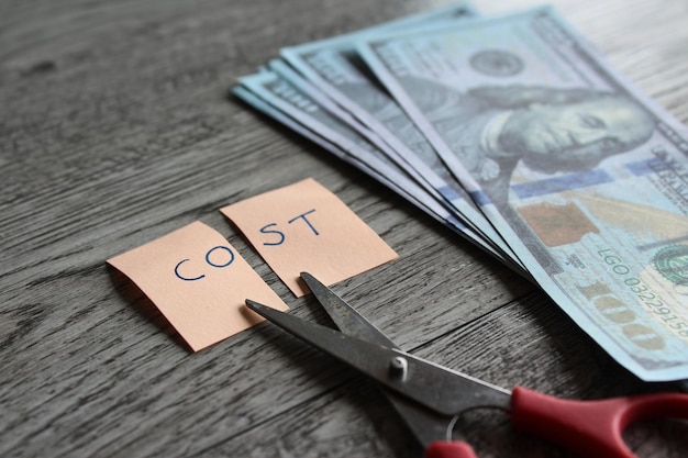 Scissor money and note with text COST Financial cost cutting reduce expenses concept