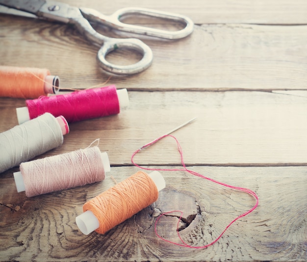 Scissors, bobbins with thread and needles. Old sewing tools on the old wooden