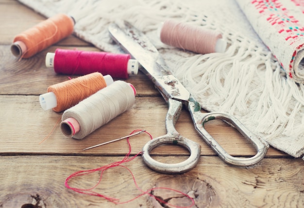 Scissors, bobbins with thread and needles, striped fabric. Old sewing tools on the old wooden