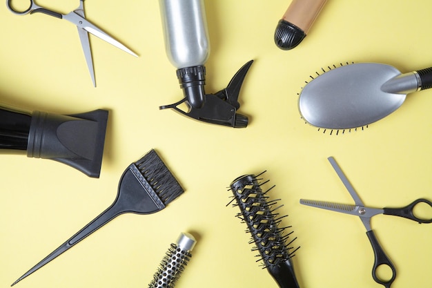 Scissors comb and other hair styling tools on yellow background