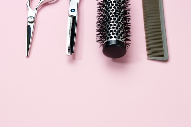 Scissors and comb on a pink background, copy space